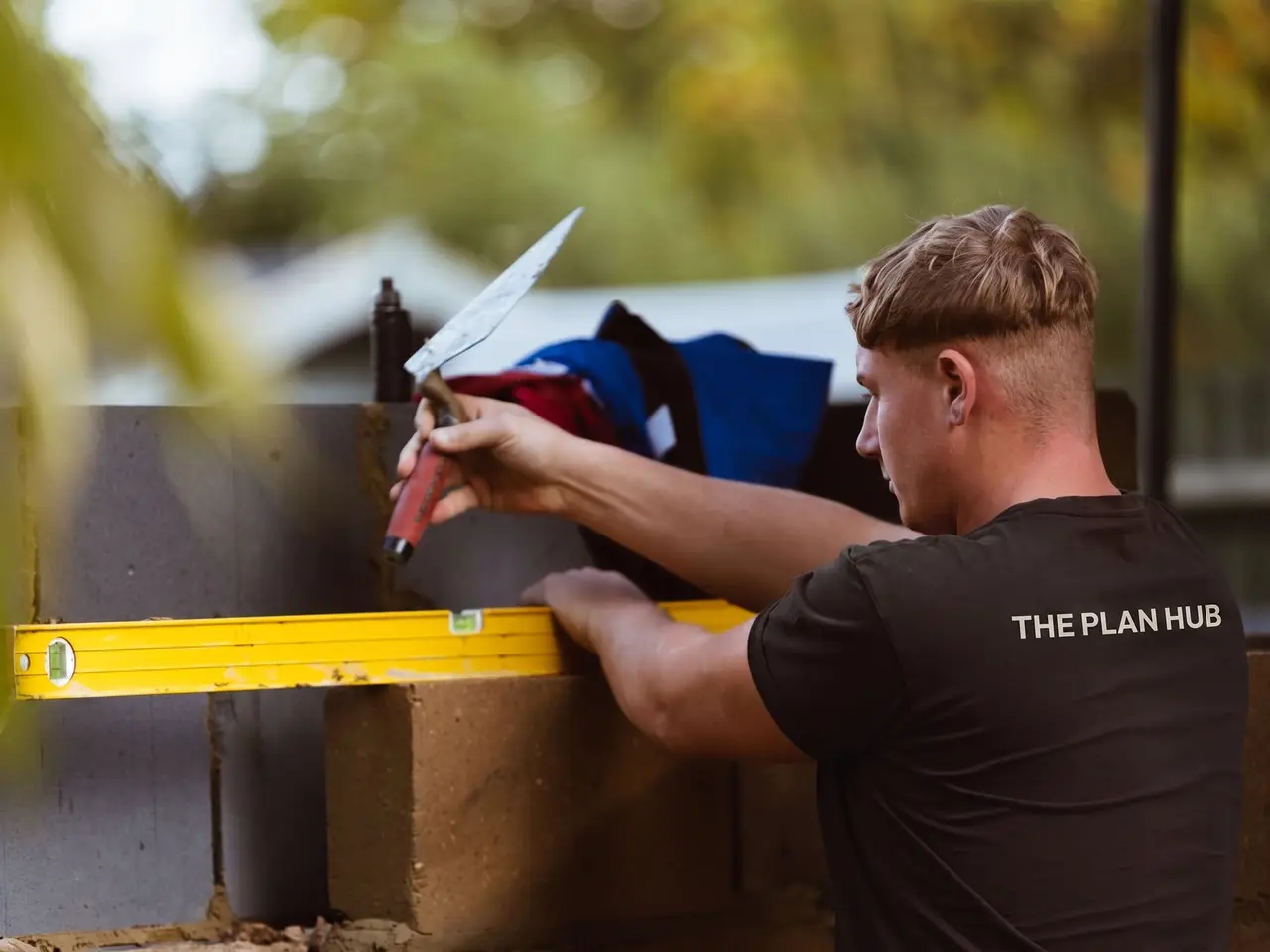 A bricklayer in a dark t-shirt printed with The Plan Hub, laying blocks on the Guildford extension